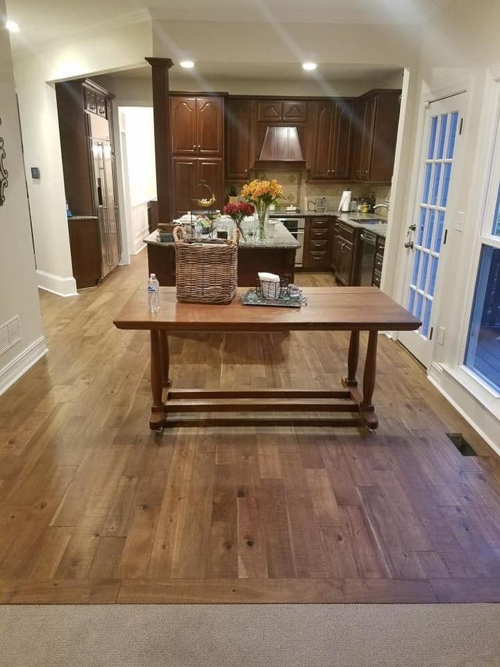 A dining room with hardwood floors and a wooden table. The kitchen is in the background.