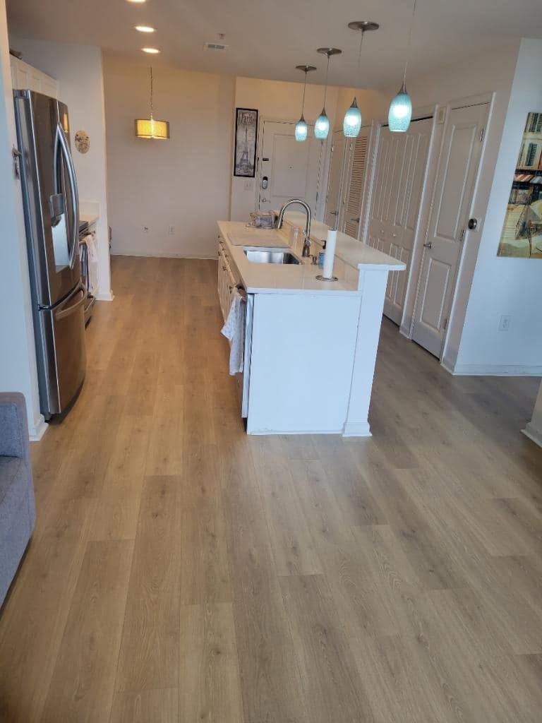 Kitchen with island, stainless steel appliances, and wood-look flooring. White cabinets and doors, pendant lights.