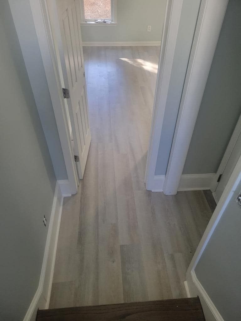 Hallway with light gray wood-look flooring, white trim and doors, and light gray walls.