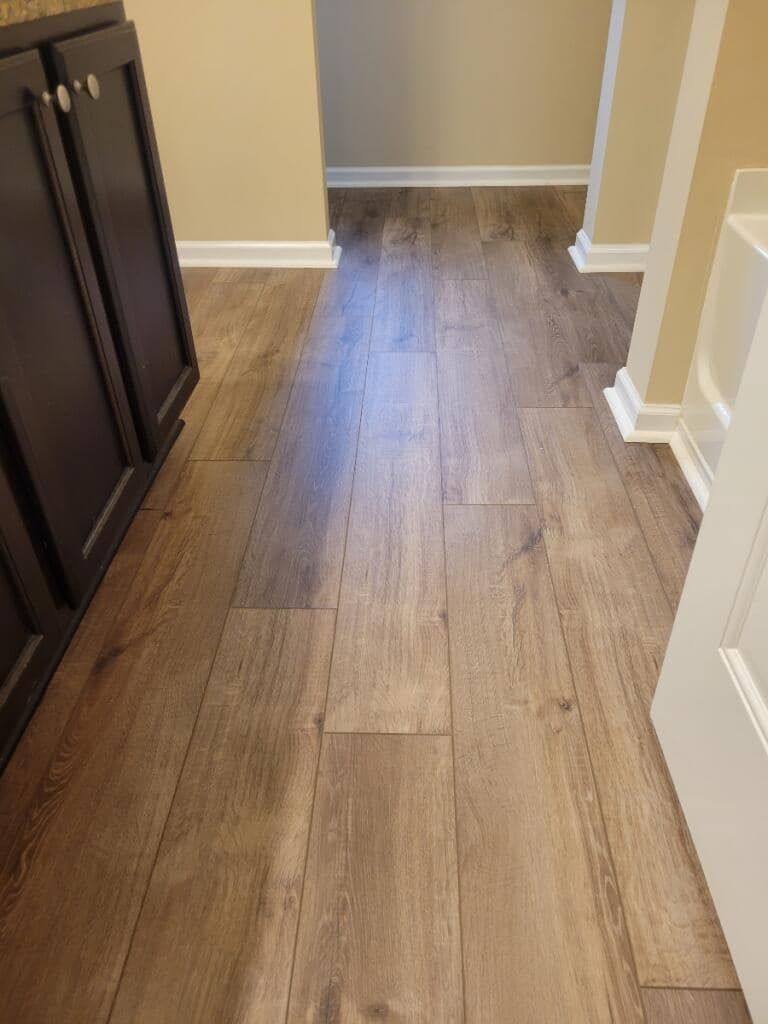 Brown wood-look flooring extends down a hallway, with dark cabinets on the left and doorways ahead and on the right.