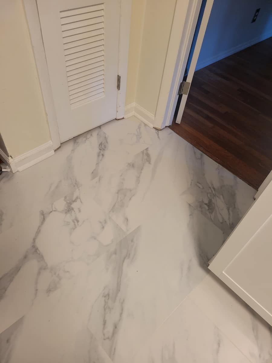 White and gray marble-patterned flooring in hallway, white door and trim, doorway to room with wood floor.