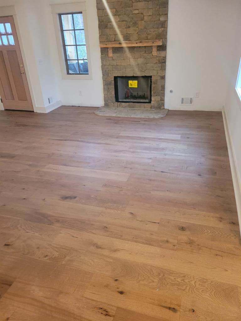 Wooden floors in a room with a stone fireplace, windows, and a wooden door.