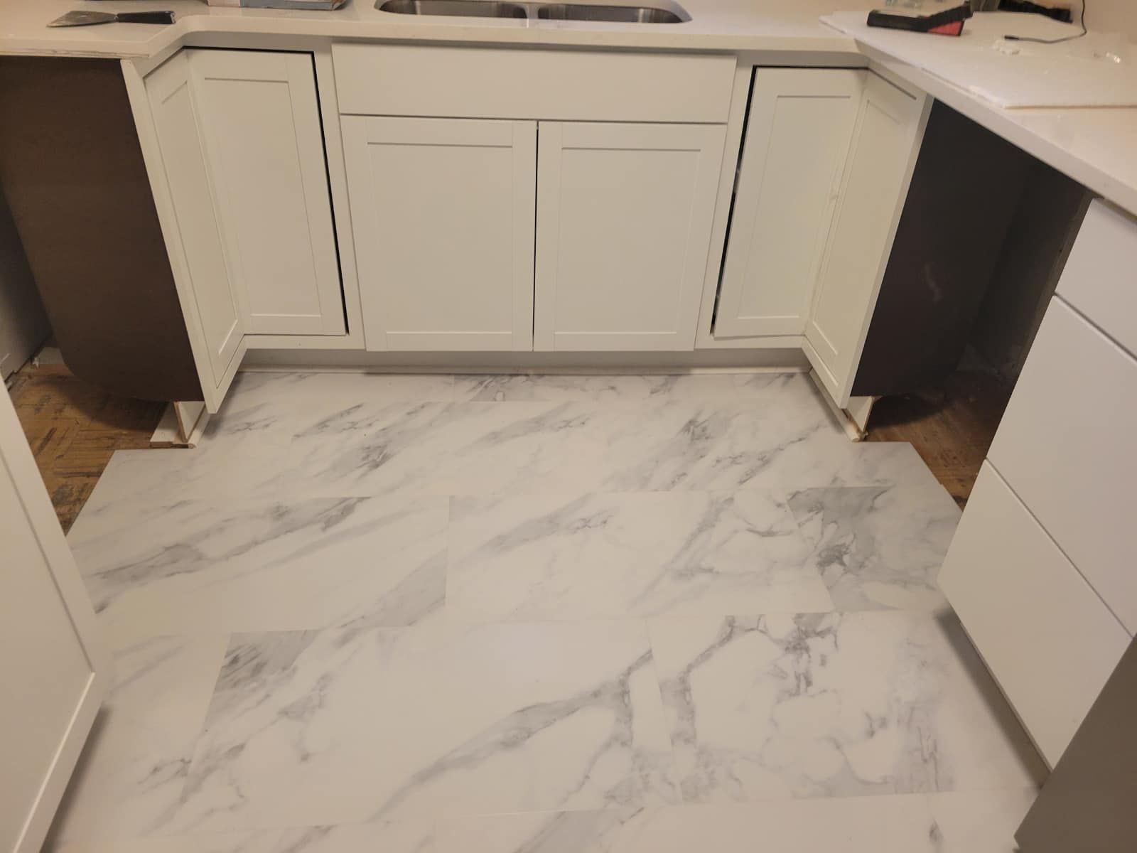 Kitchen with white cabinets, light-colored marble-look tile flooring. Partially installed cabinets and counter.