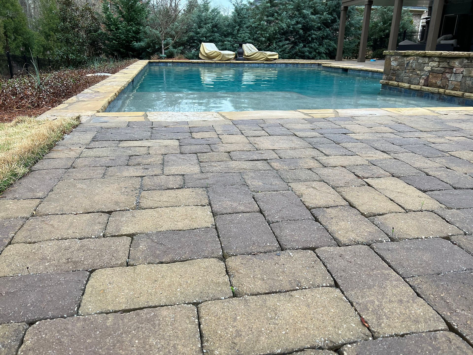 A brick walkway leading to a large swimming pool.