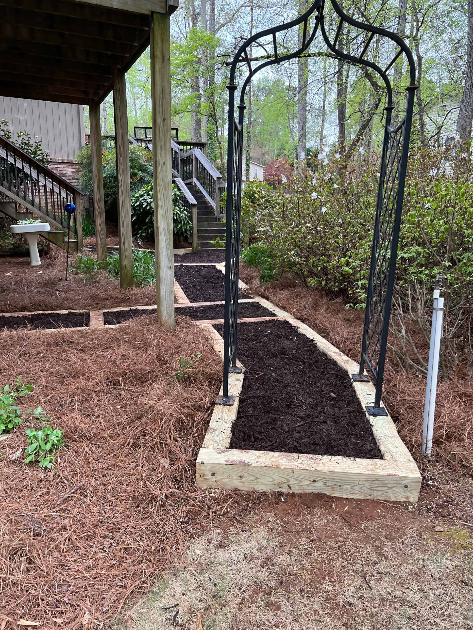 A garden path with a metal arch and steps leading to a deck.