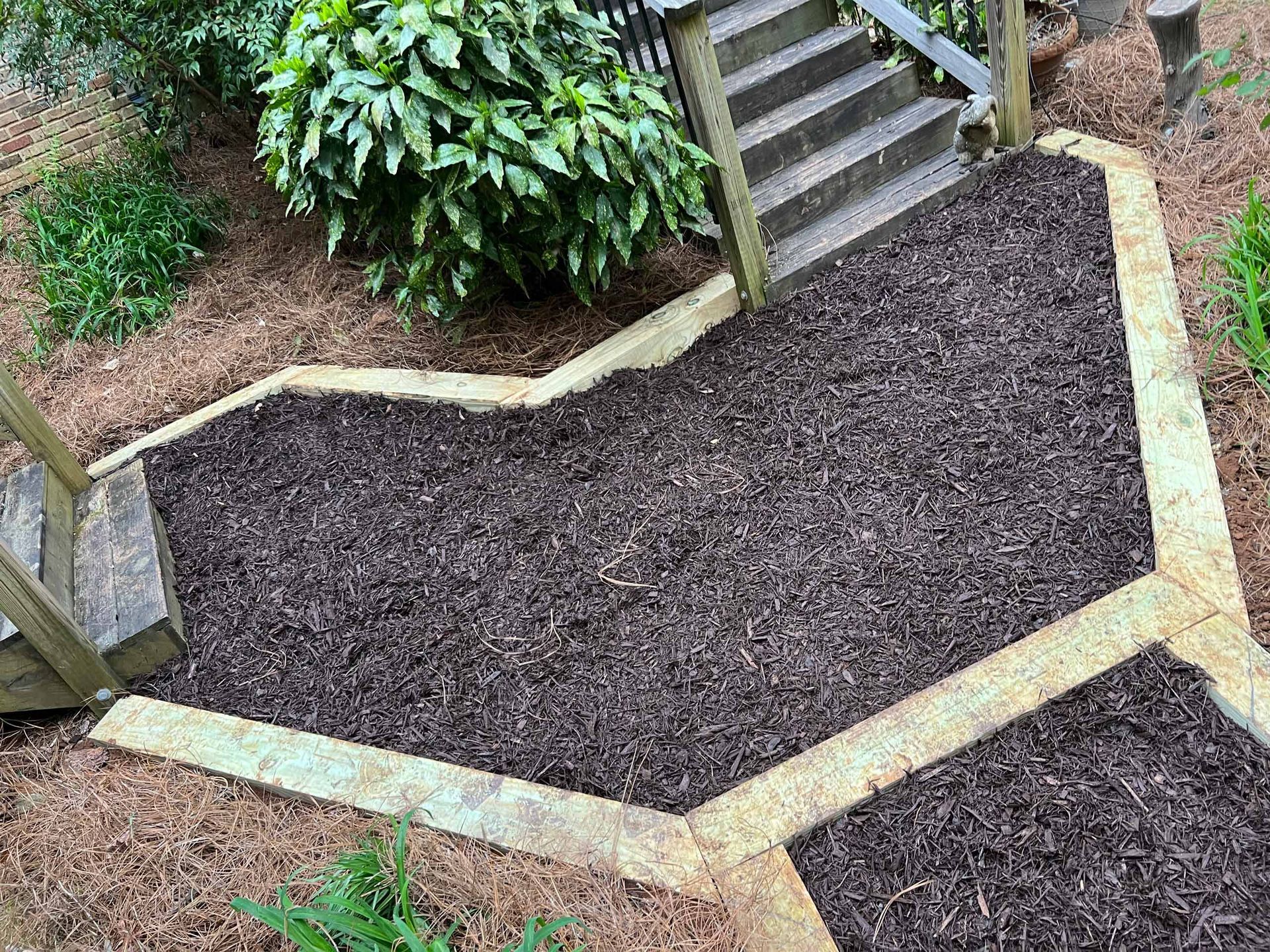 A wooden walkway surrounded by mulch and stairs in a garden.