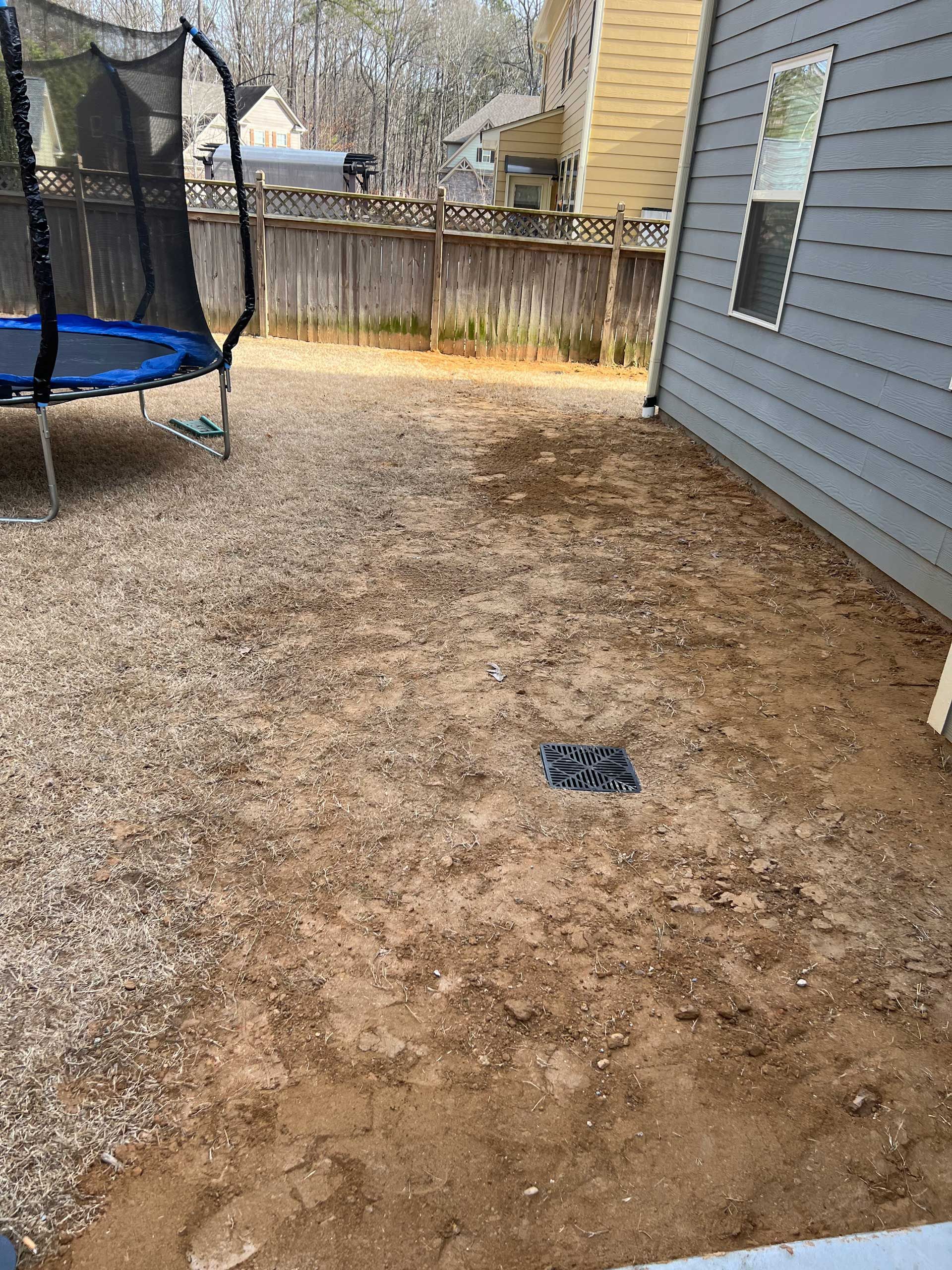 A trampoline is sitting in the dirt in front of a house.