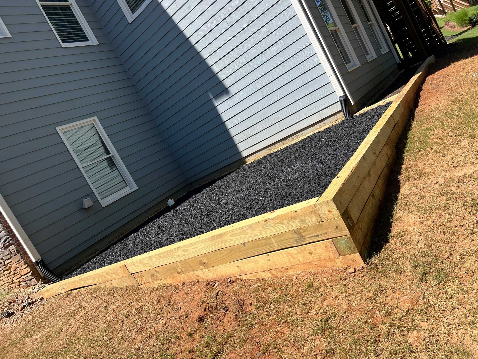 A house with a wooden fence and gravel in front of it.
