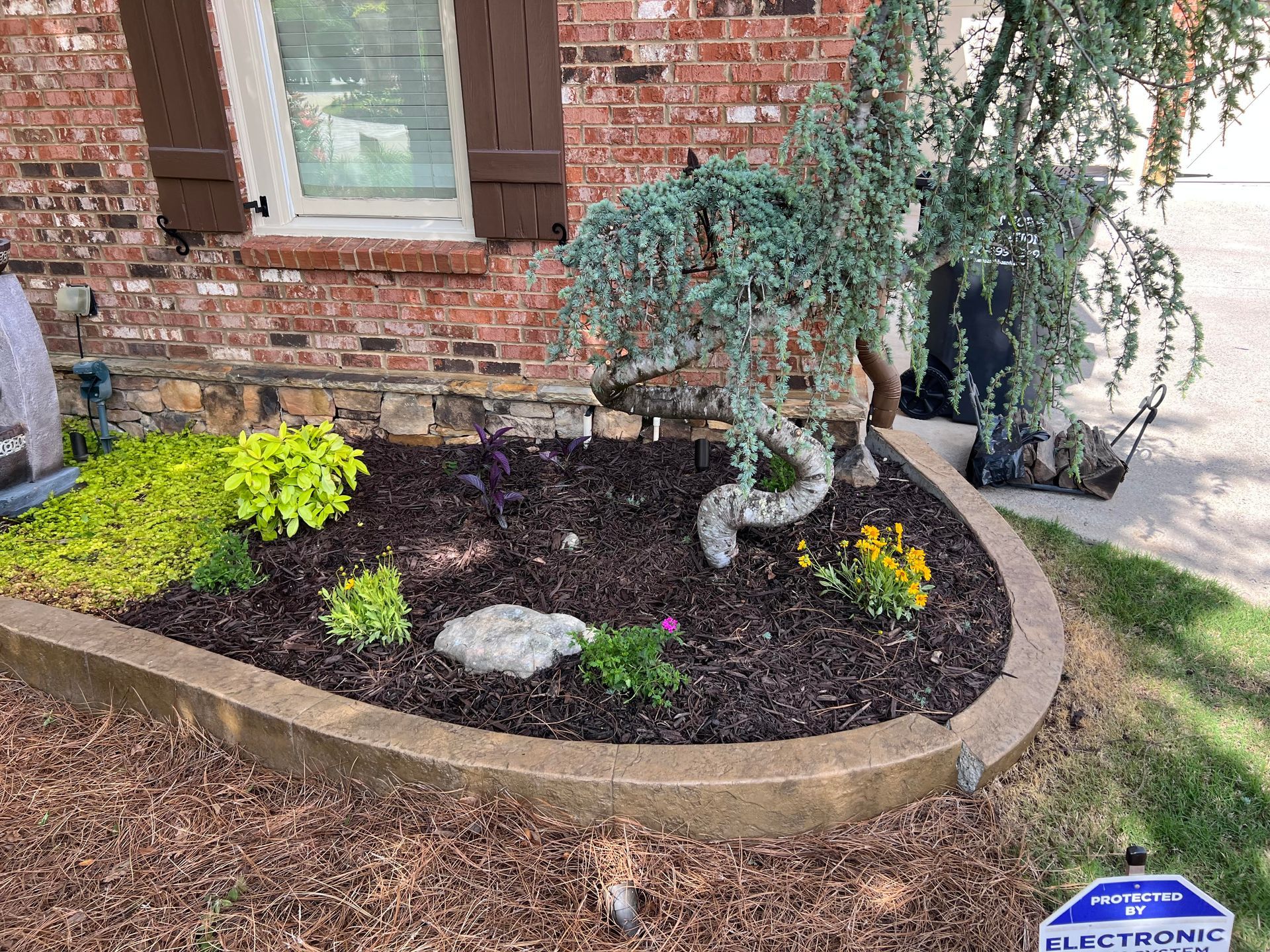 A garden with flowers and rocks in front of a brick house.