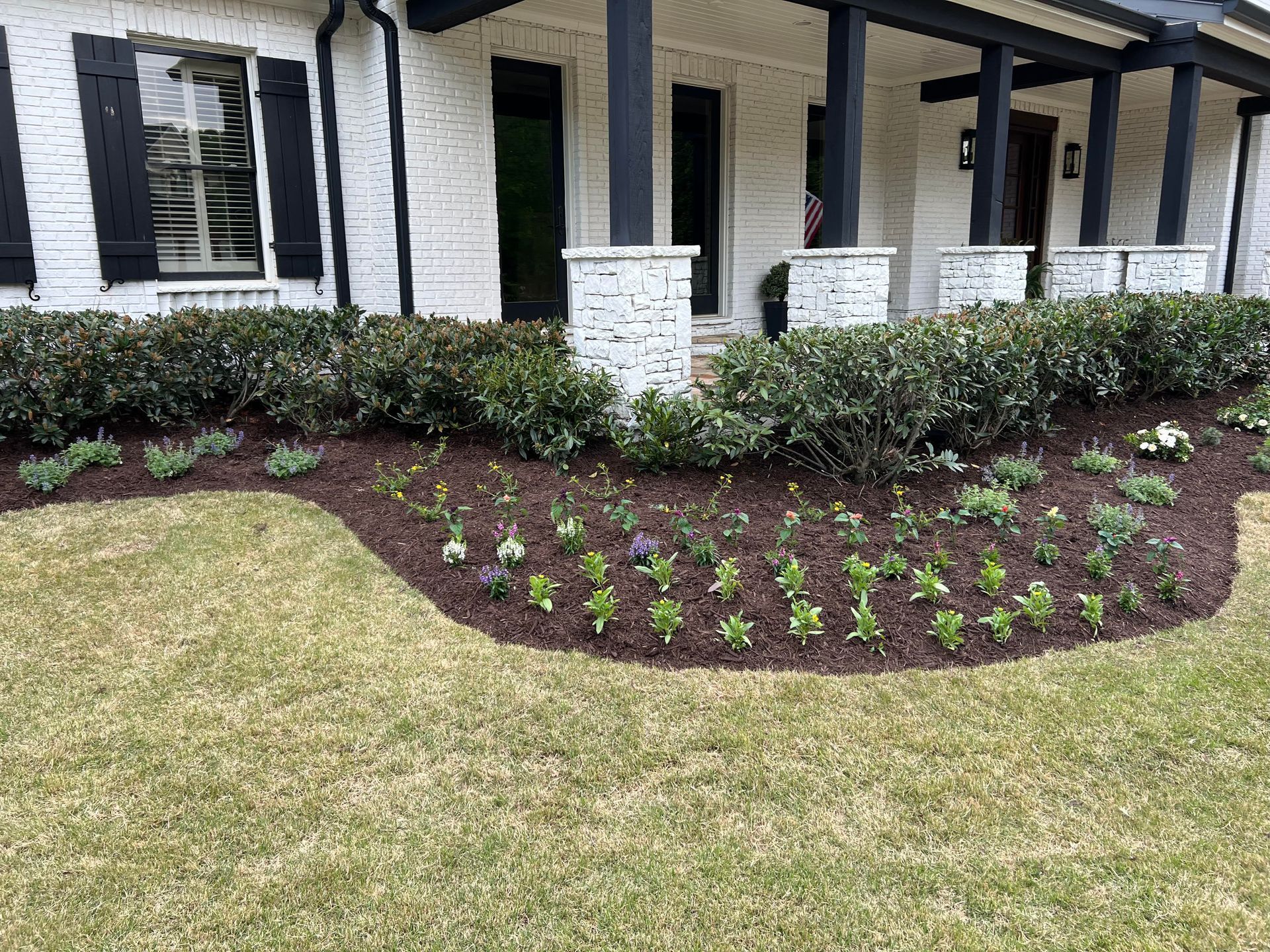 A white house with black shutters and a lush green lawn in front of it.