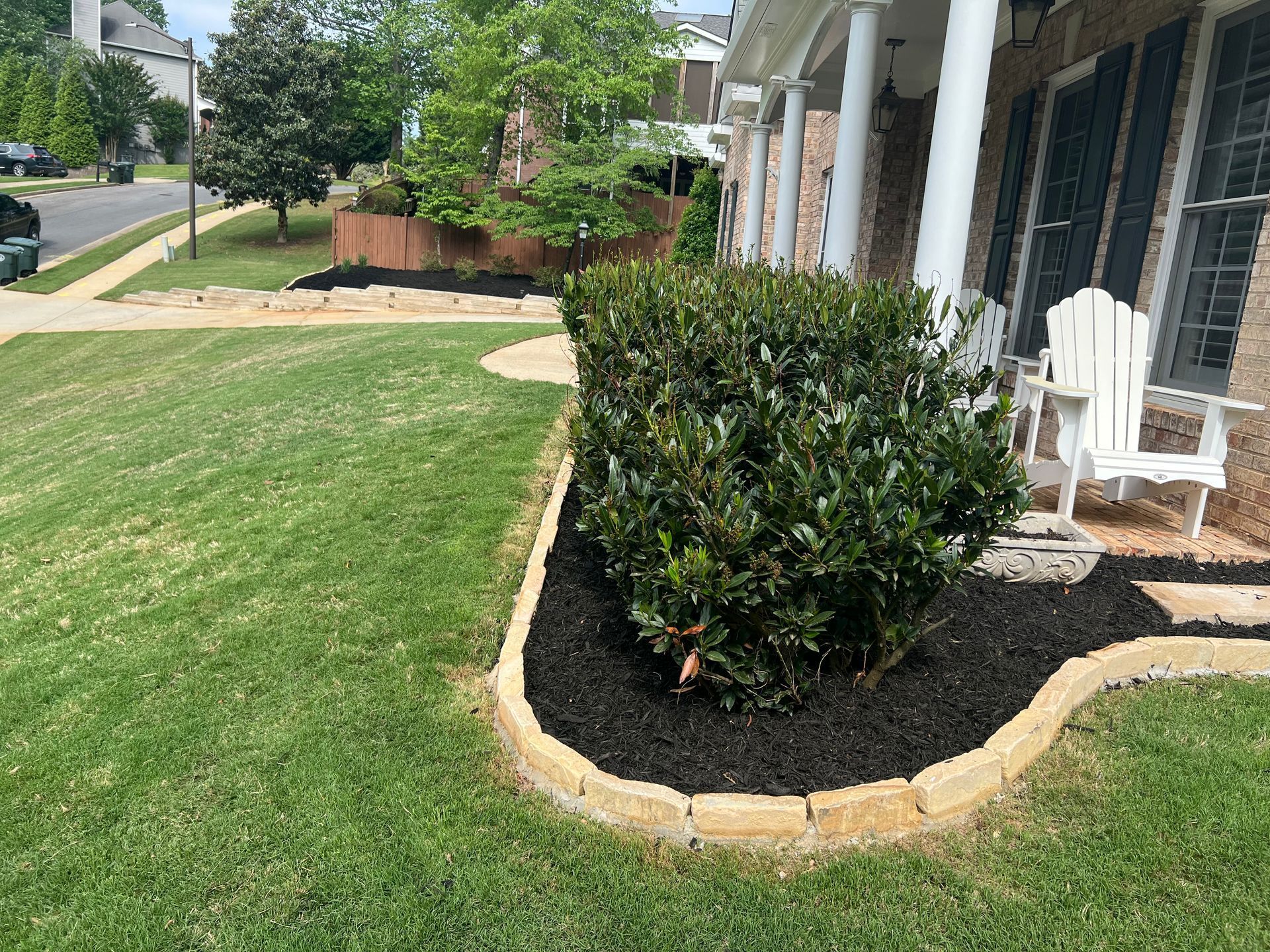A lawn with a bush and two chairs in front of a house.