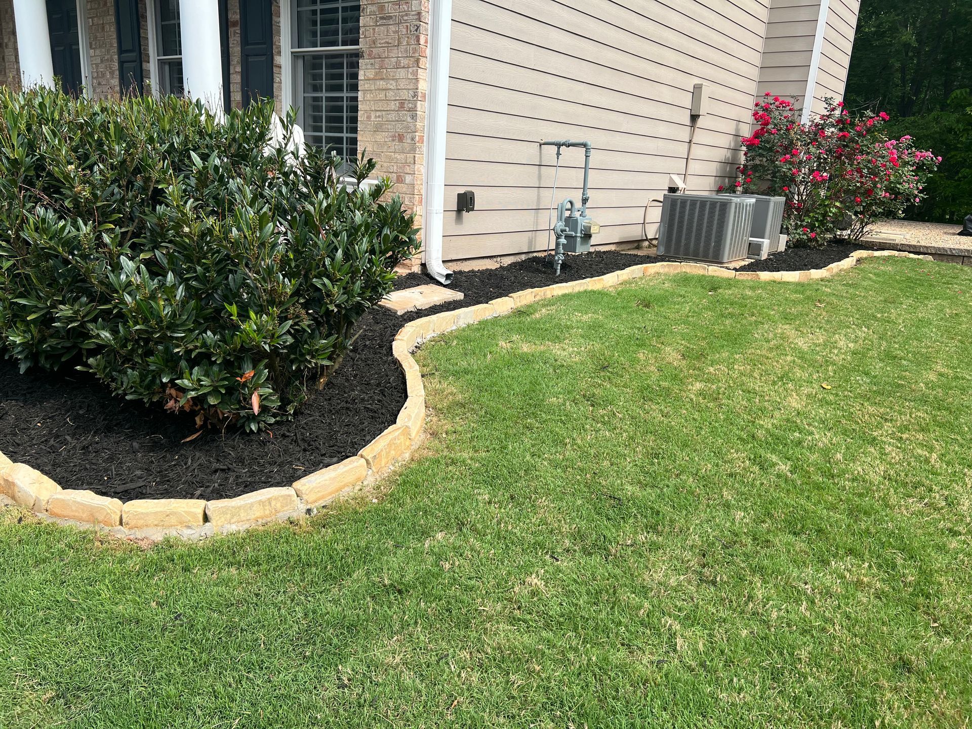 A lush green lawn with a brick curb in front of a house.