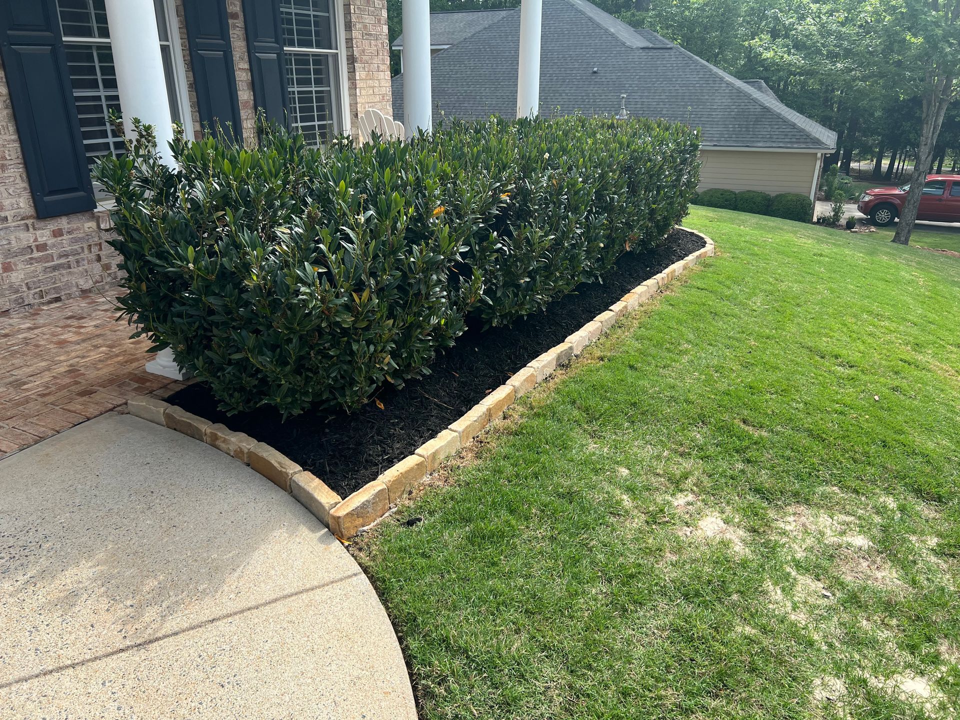 A brick house with a lush green lawn and bushes in front of it.