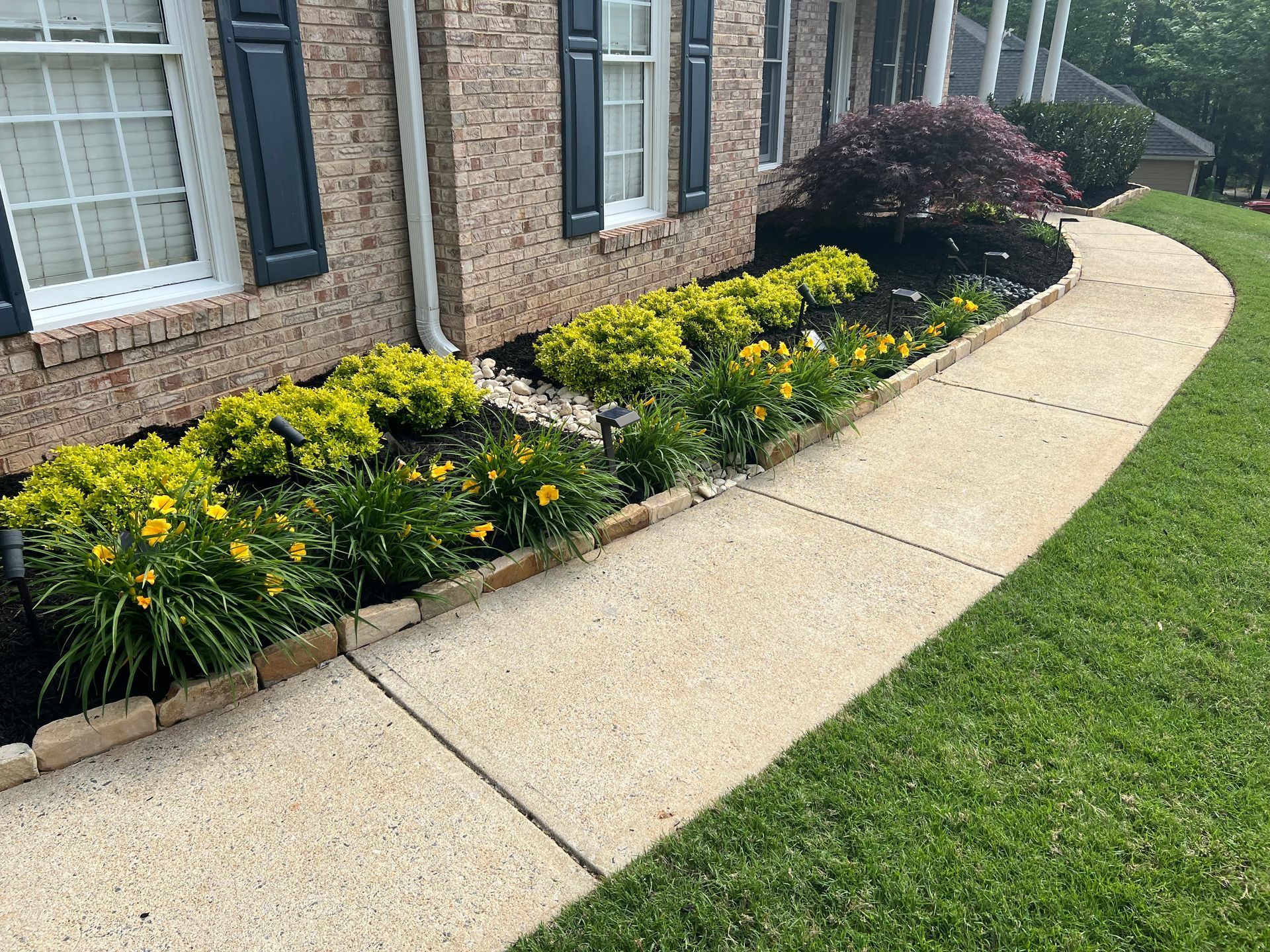 A sidewalk leading to a brick house with flowers in front of it.