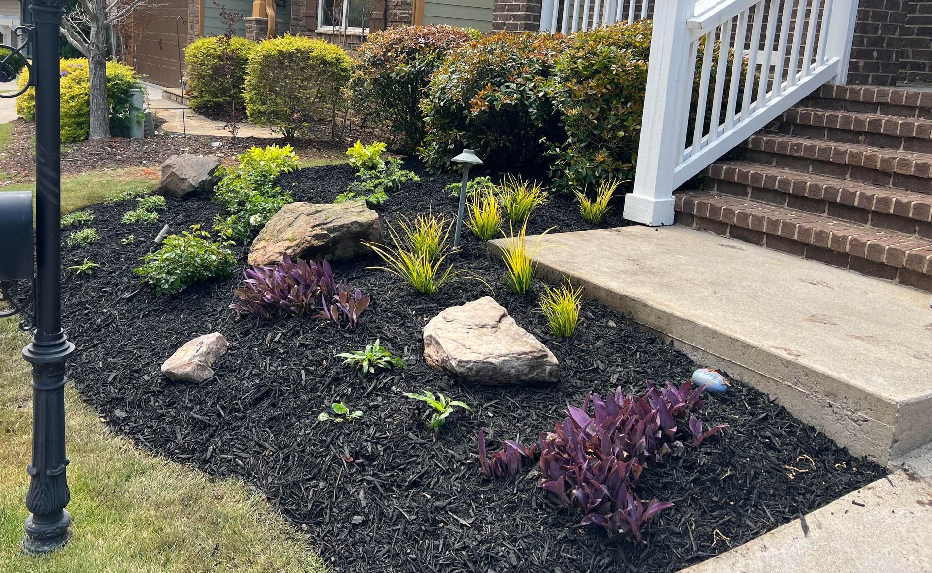 A lush green garden in front of a house with stairs and a mailbox.