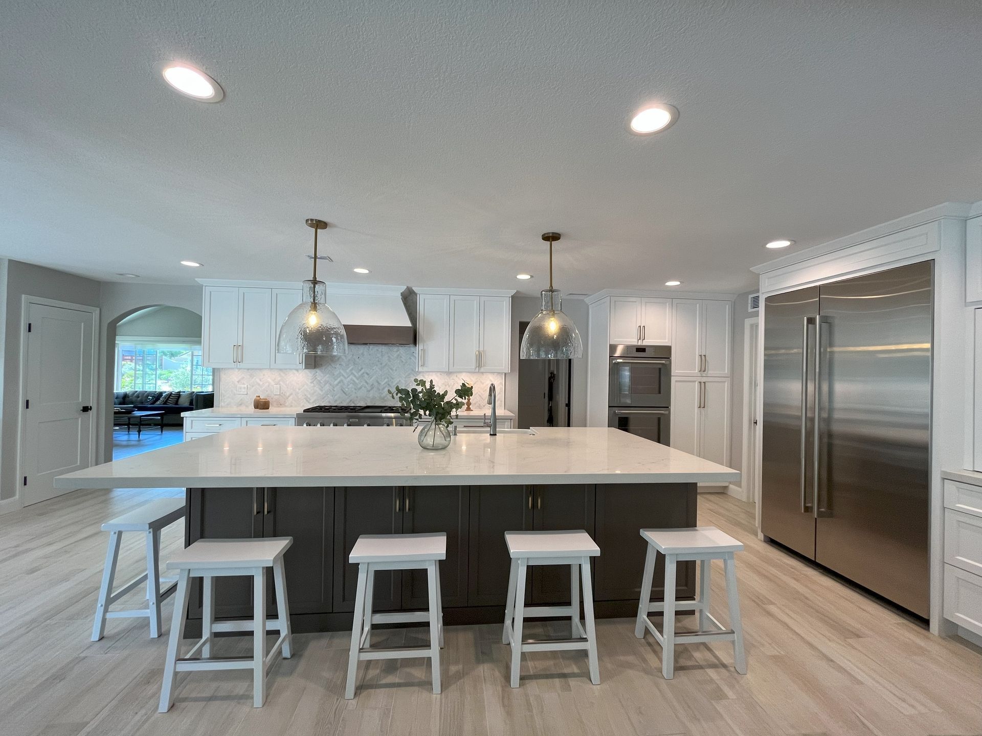 Modern kitchen with a gray island, white cabinets, stainless steel appliances, and wood floors.