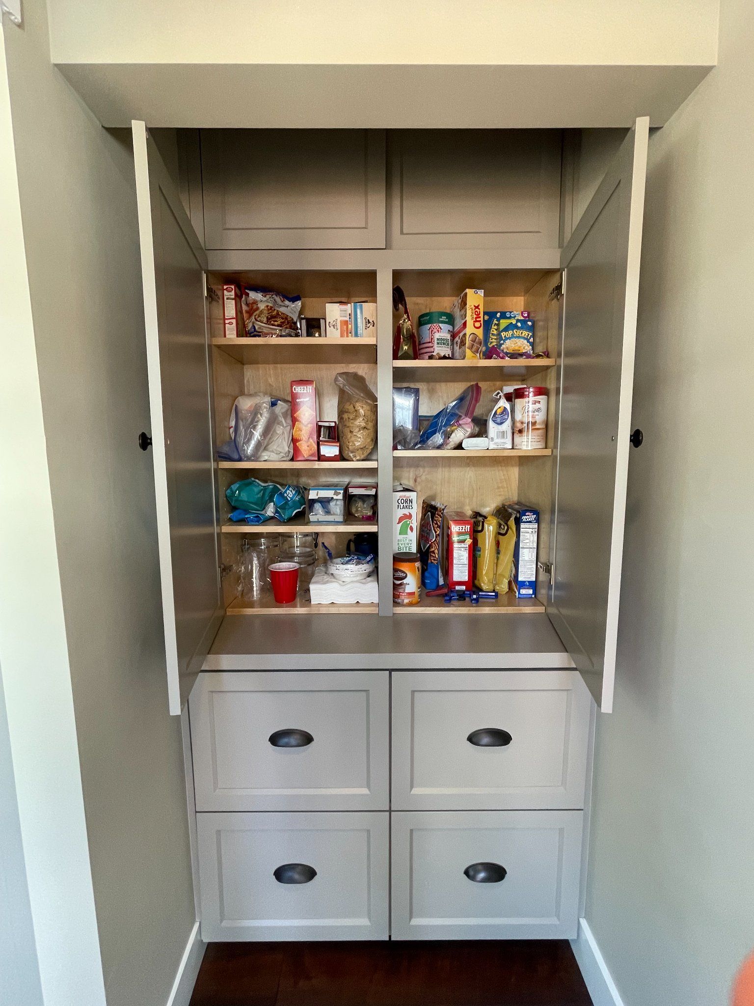 Built-in pantry with light gray cabinets and black hardware. Shelves and drawers store various food items.