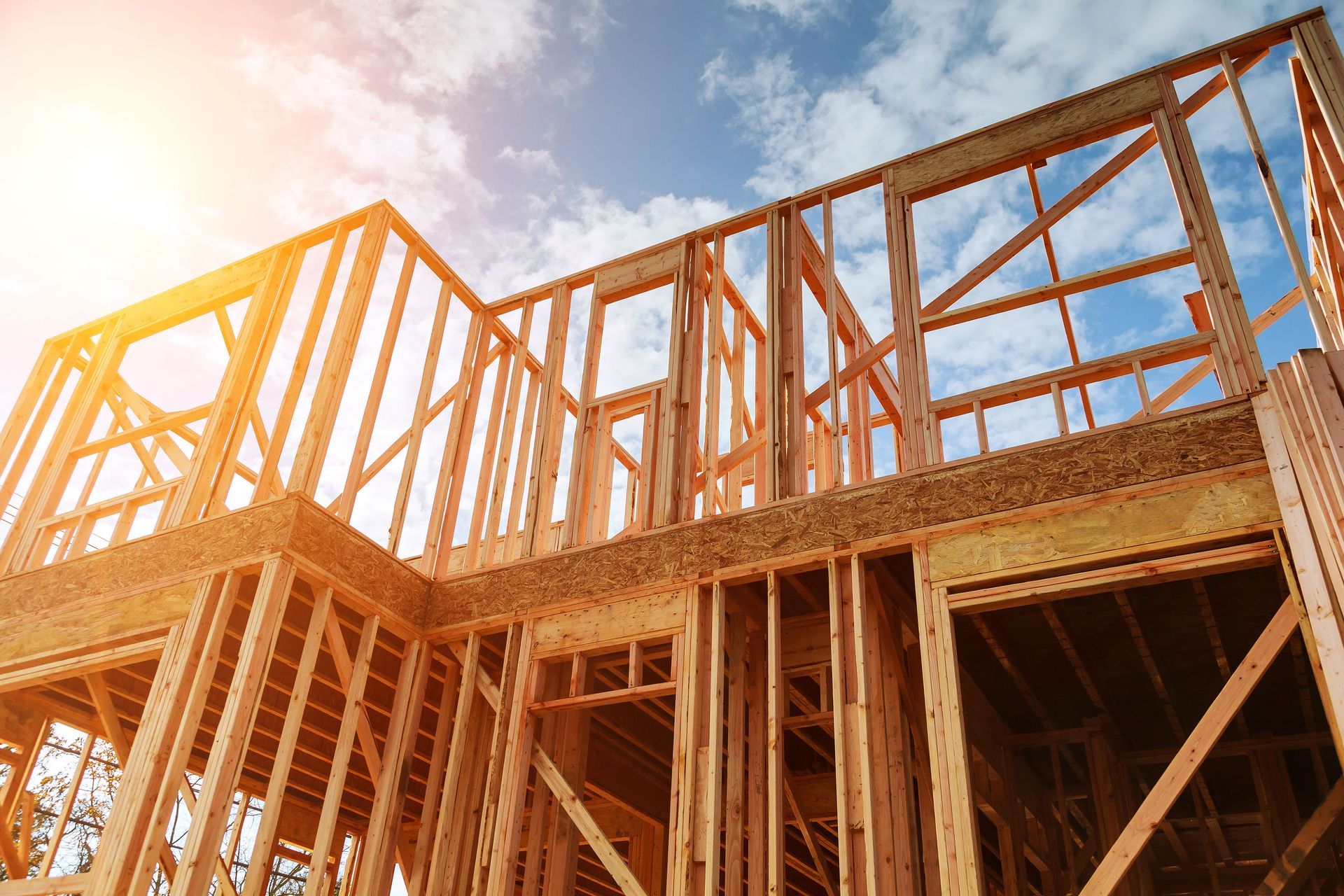 Wooden frame of a house under construction against a blue sky with sunlight.