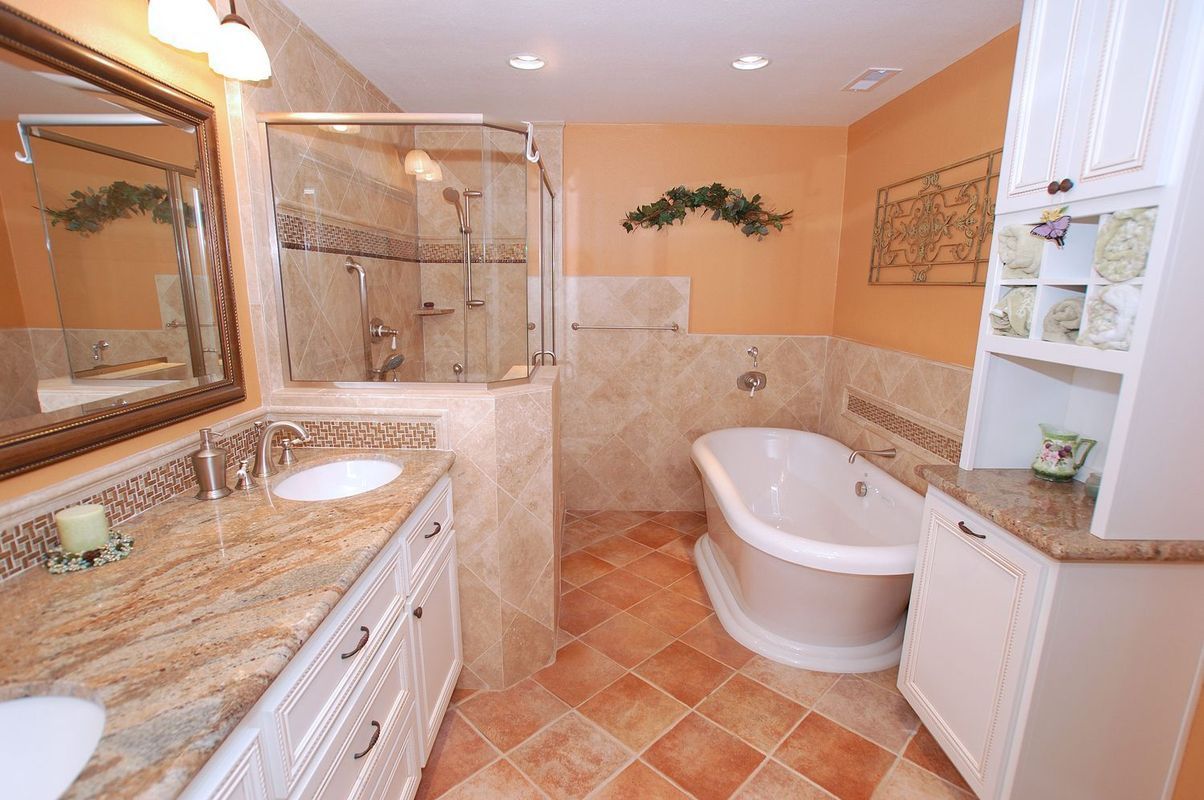 Bathroom with marble countertop vanity, freestanding tub, glass shower, and orange walls.