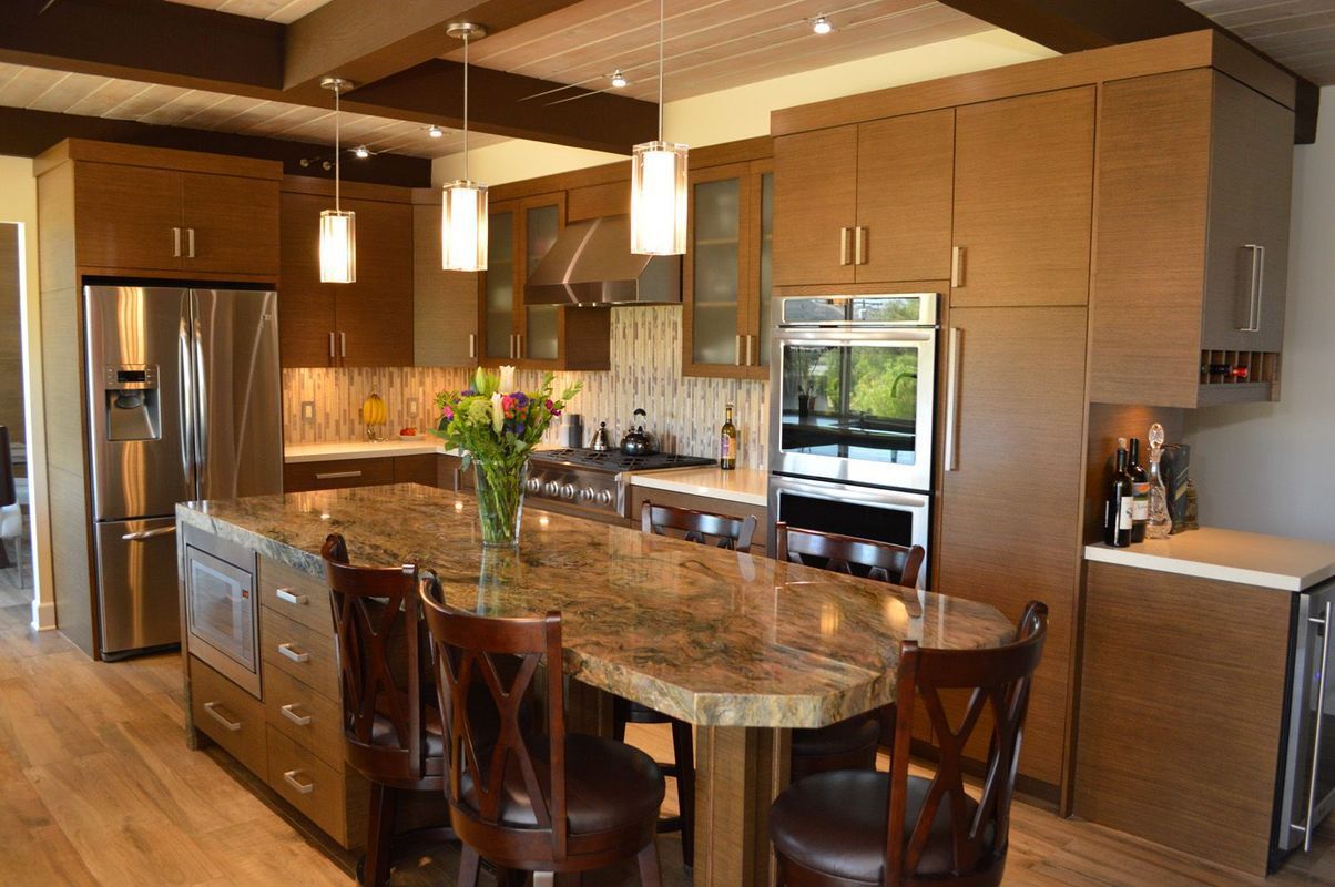 Modern kitchen with brown cabinets, large island, stainless steel appliances, and wood flooring.