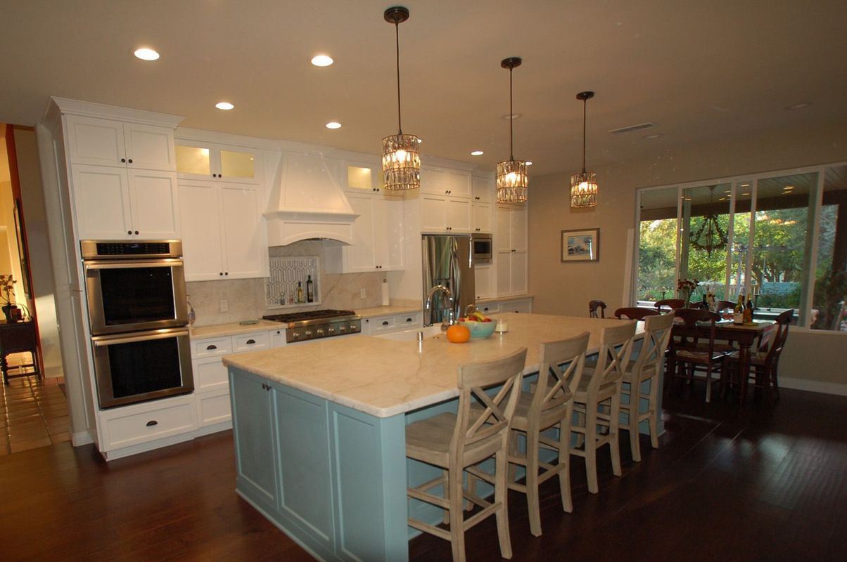 Spacious kitchen with blue island, white cabinets, dark wood floors, and dining area.