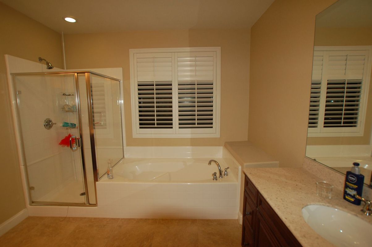 Bathroom with shower, tub, vanity, and window with blinds; beige walls and floor.
