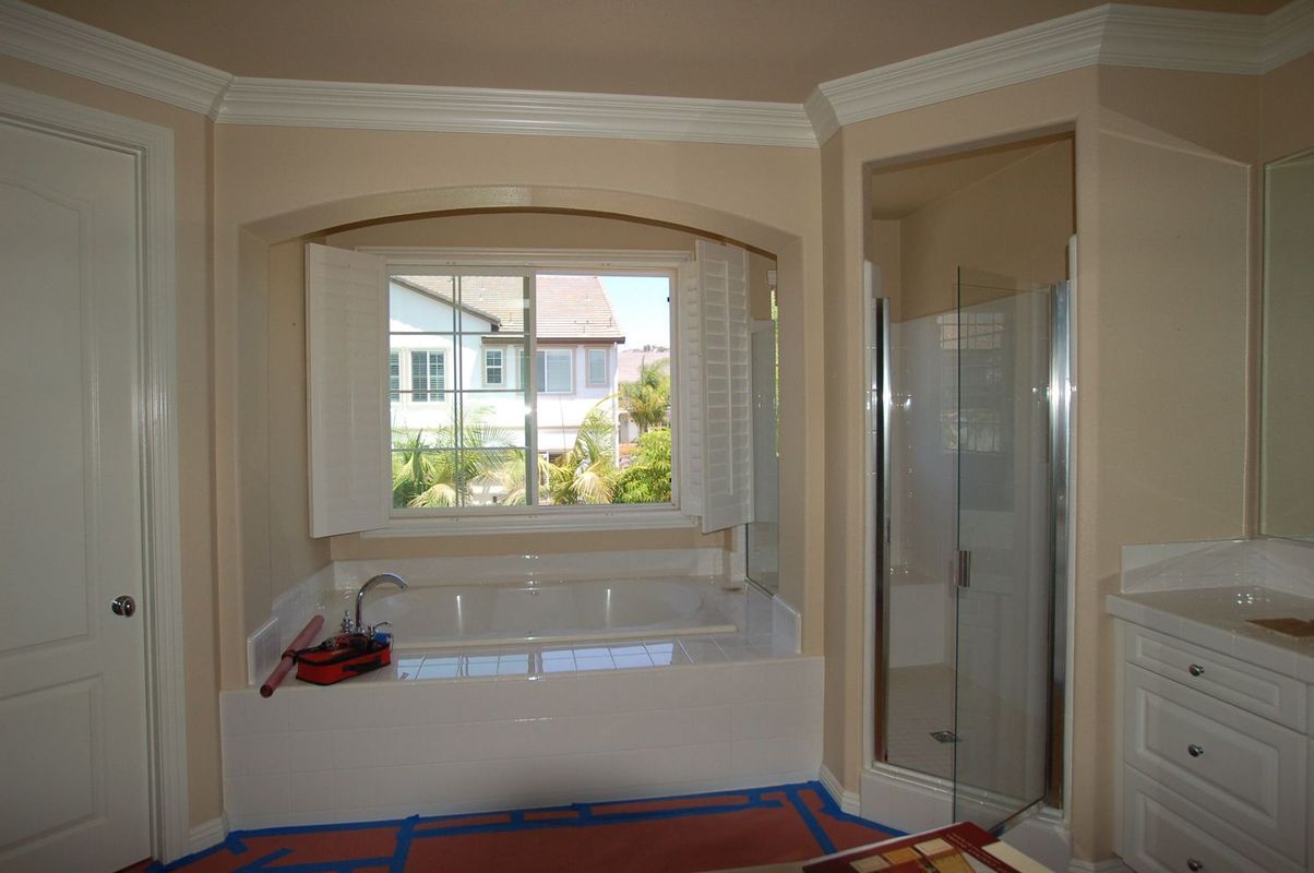 Bathroom with window over a tub, shower, and white vanity. Beige walls, white trim.