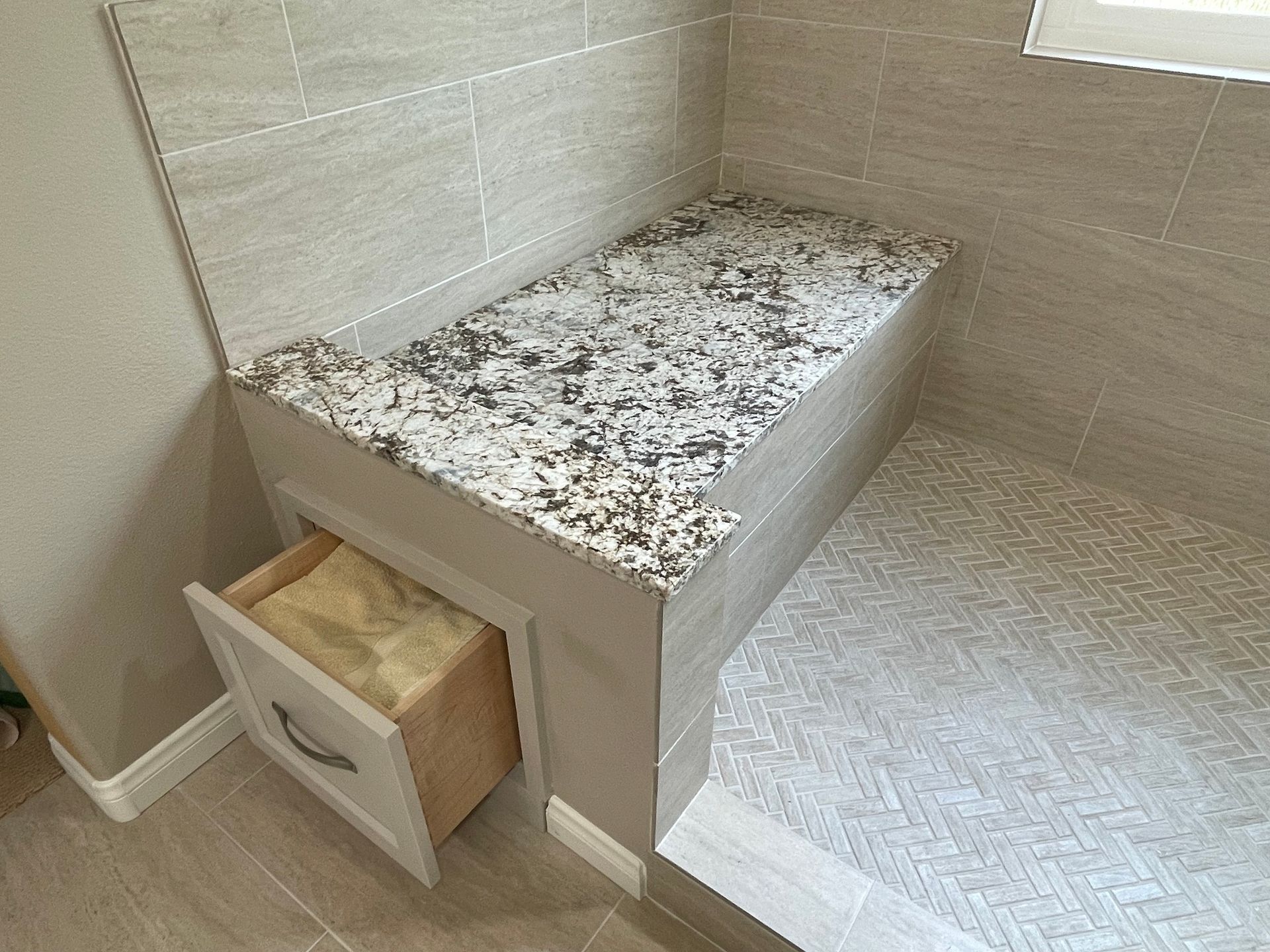 Shower with granite-topped bench, tile walls, and a drawer. Light gray and white tones.