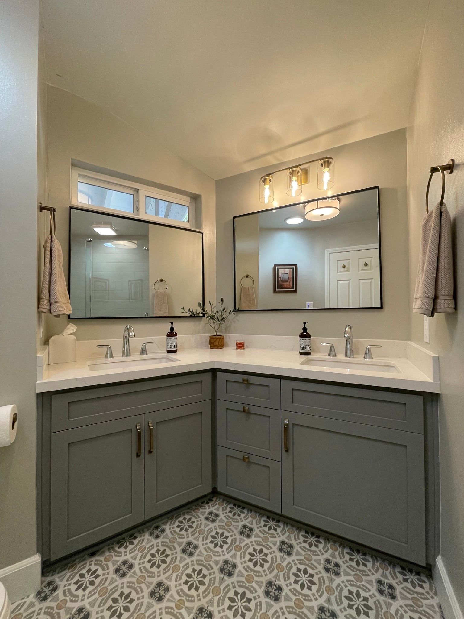 Gray bathroom with corner vanity, two mirrors, decorative floor tiles, and a window.