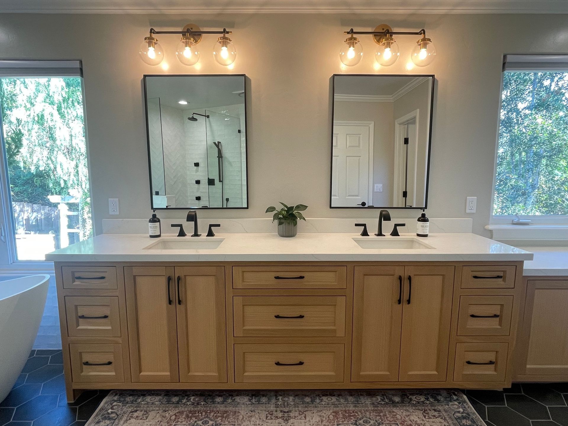Bathroom vanity with two mirrors, light fixtures, and sinks; wood cabinets, neutral walls, and rug.