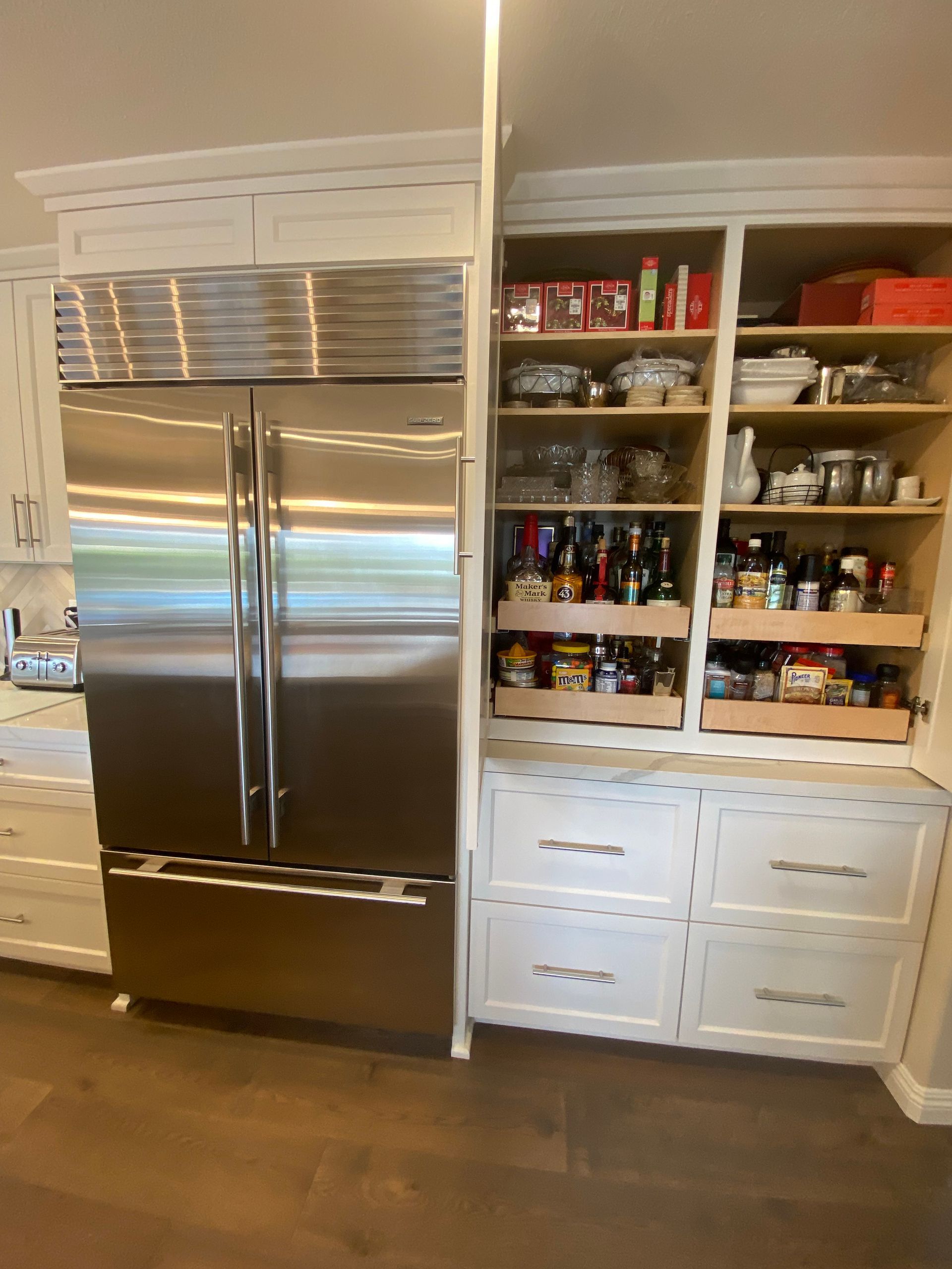 Stainless steel refrigerator next to a built-in pantry with shelves and drawers. The pantry is filled with food items.