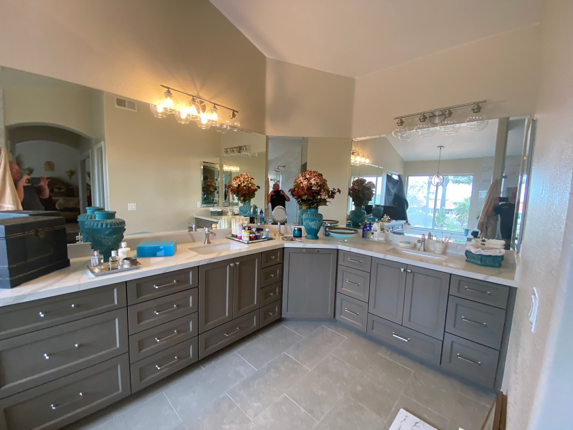 Bathroom with two sinks, gray cabinets, large mirrors, and decorative items.
