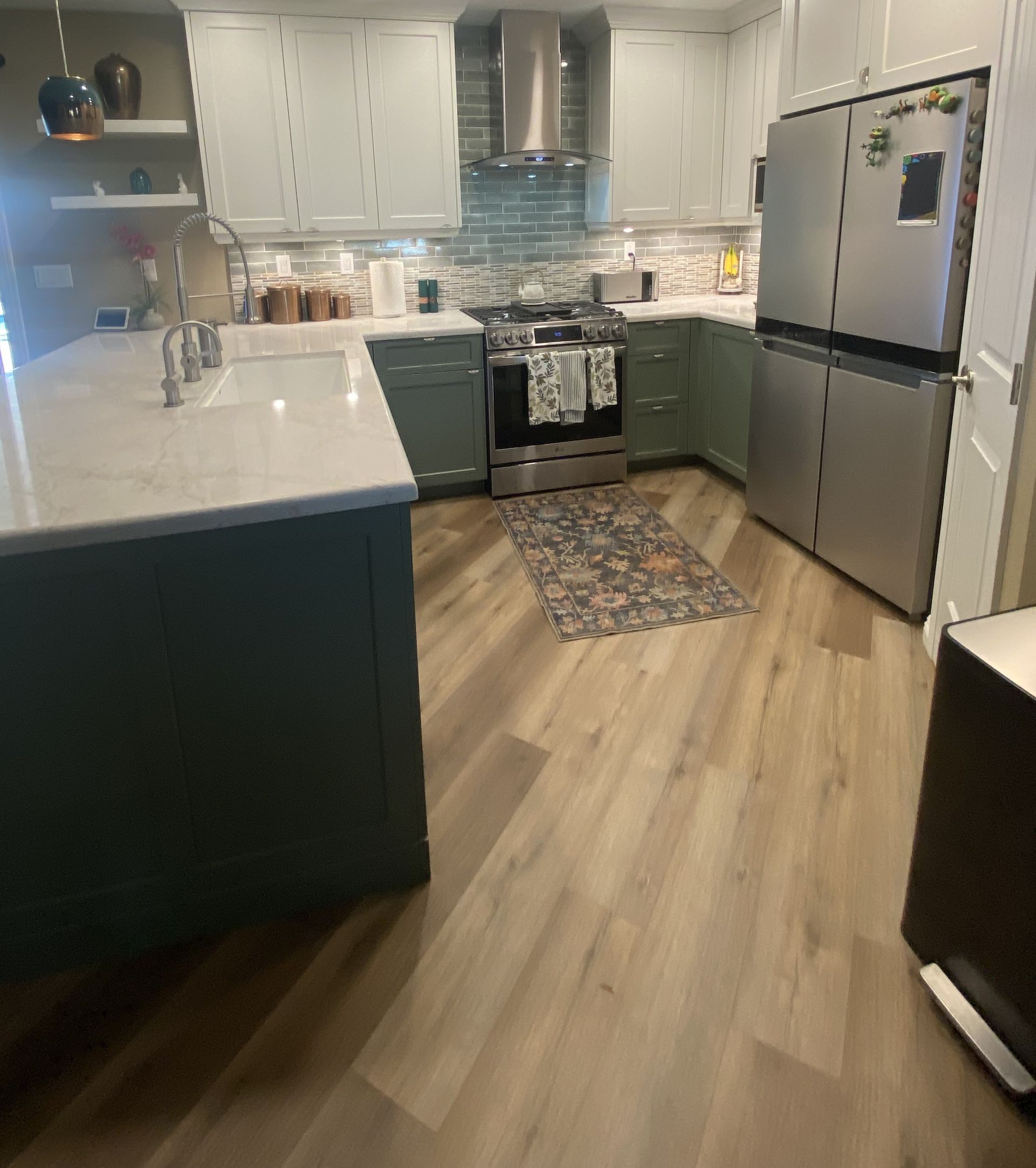 Kitchen with sage green and white cabinets, stainless steel appliances, and wood-look flooring.