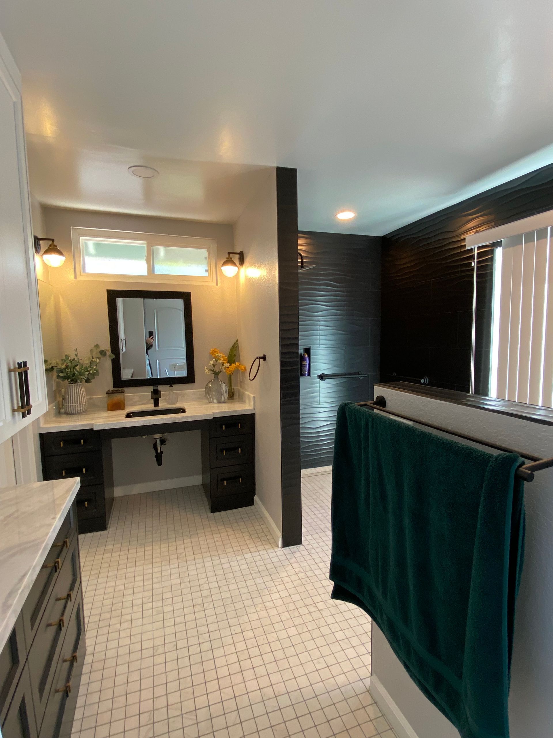 Bathroom with a black vanity, dark tiled shower, and white tile floor. A green towel hangs on a bar.