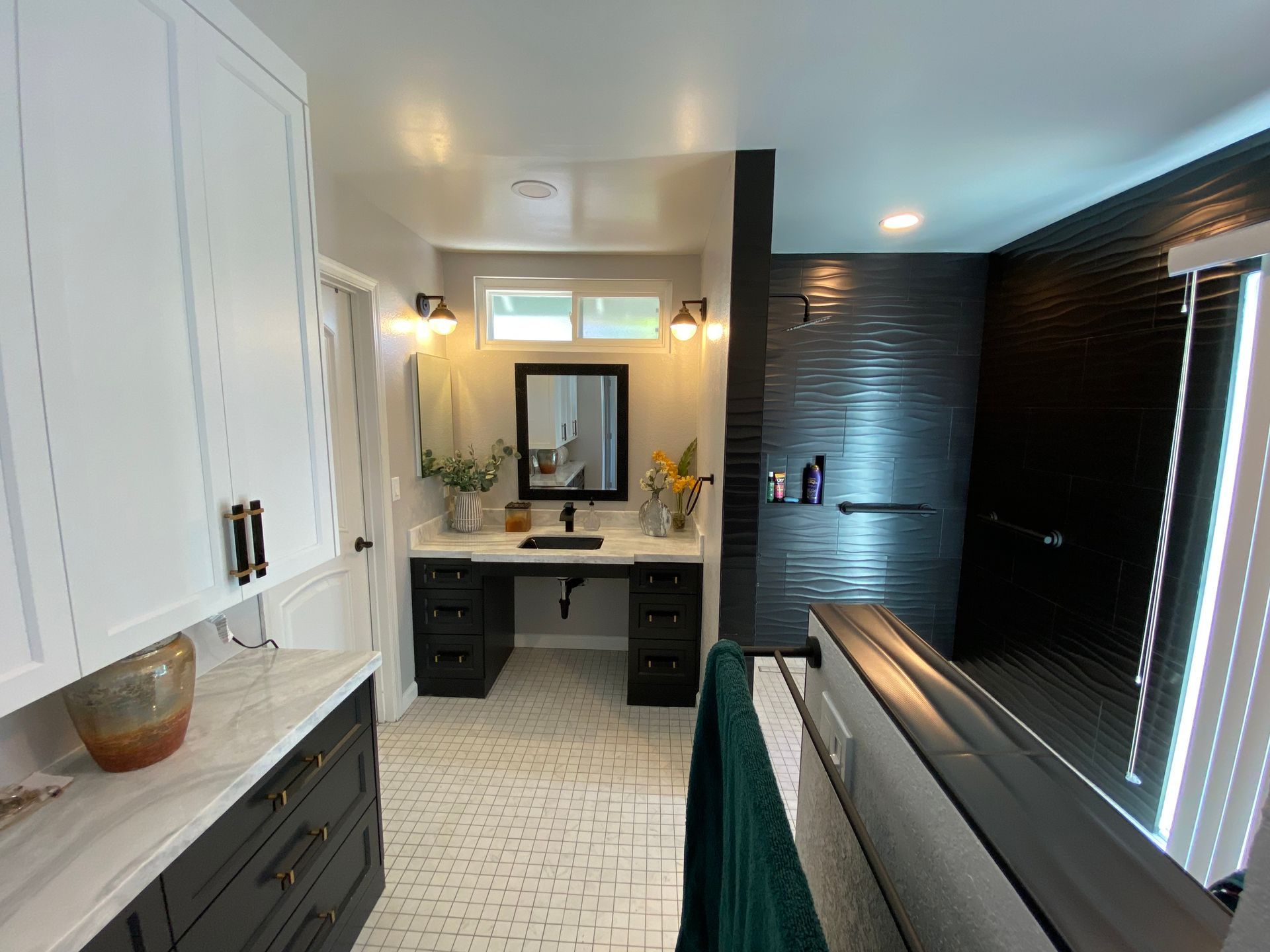 Bathroom with black and white accents. Black vanity, dark tiled shower, white cabinets, light tile floor.