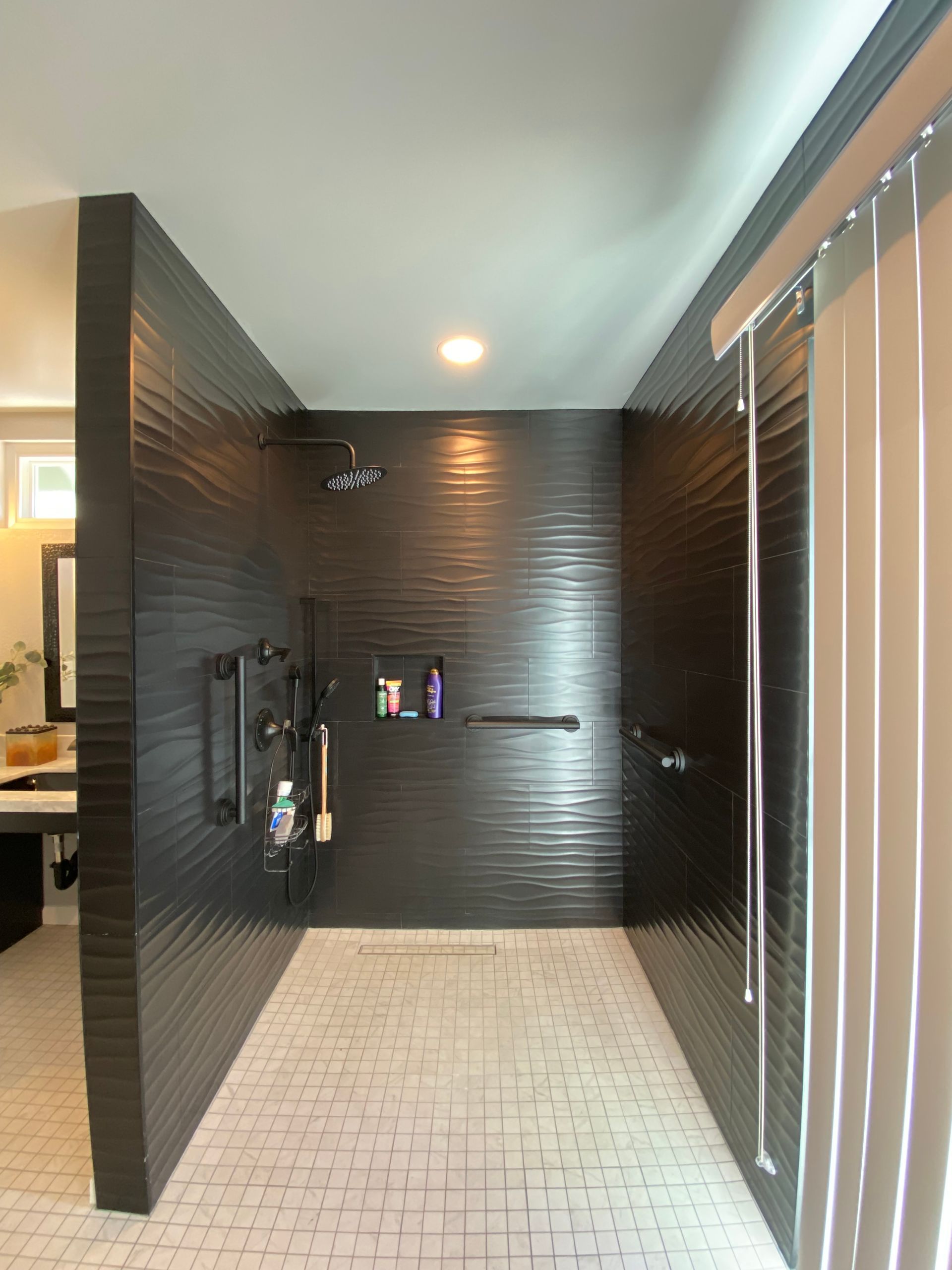 Black tiled shower with white floor, multiple showerheads, and grab bars.