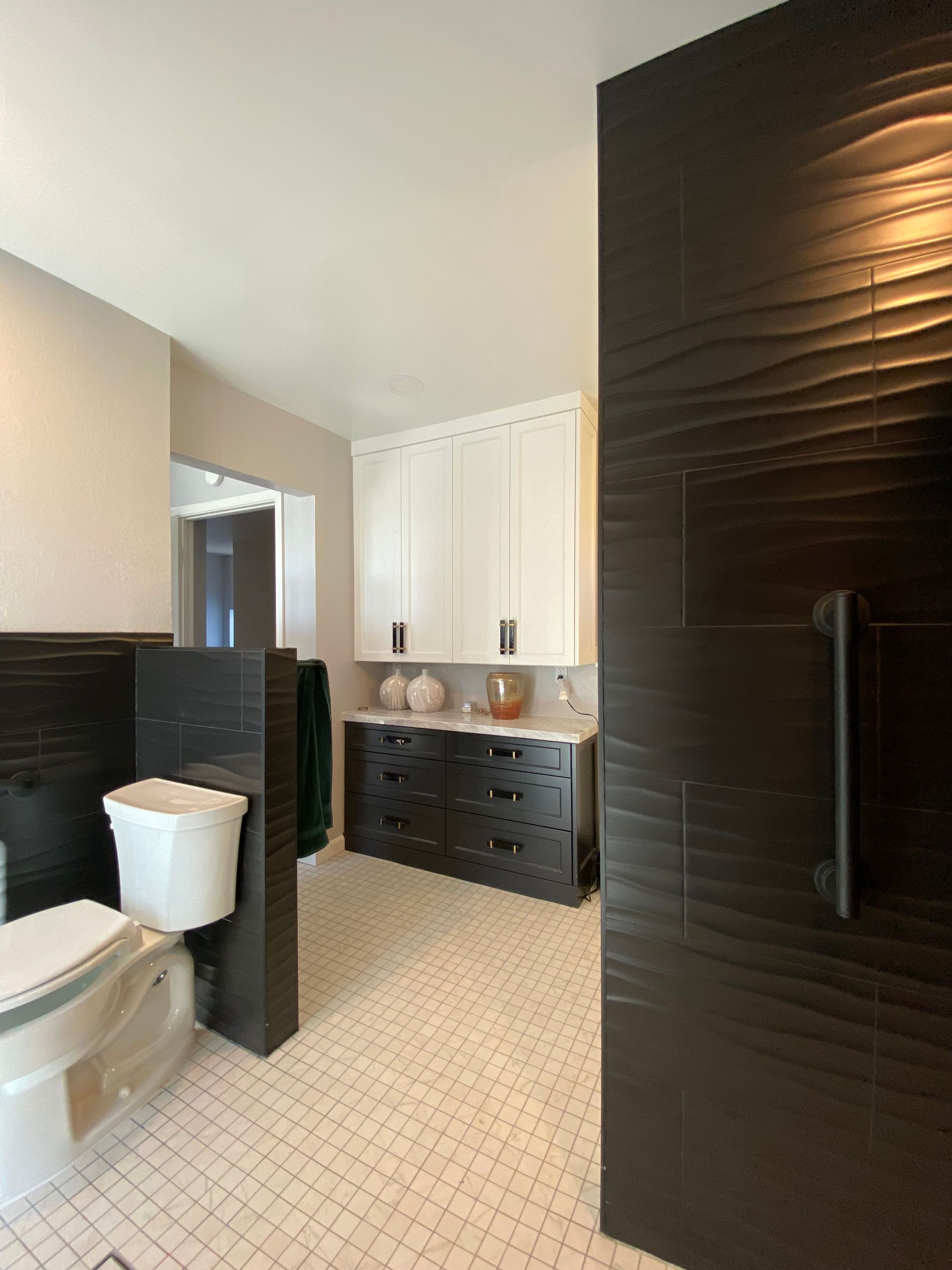 Bathroom with black and white cabinetry and textured black shower door. White tiled floor.