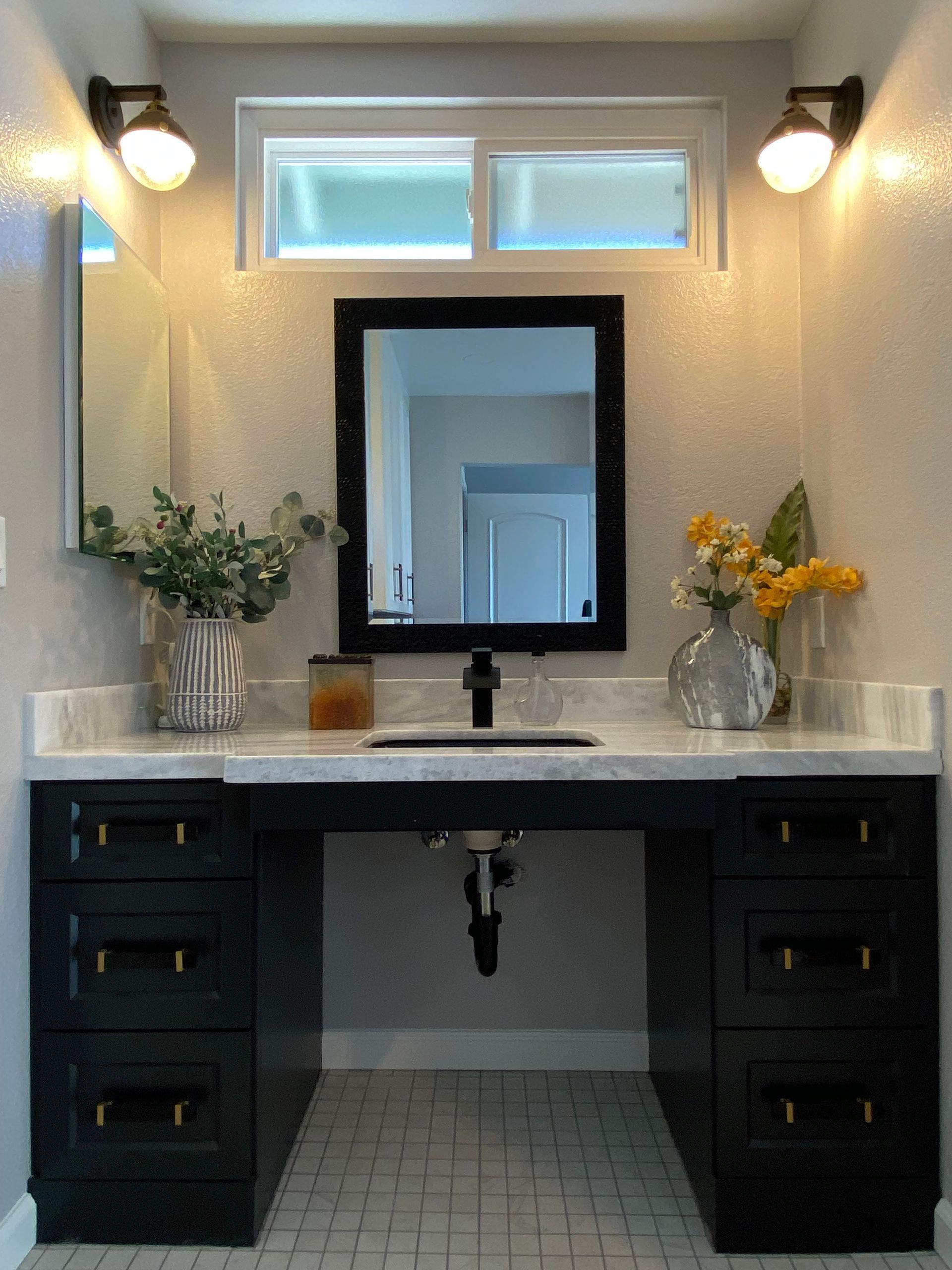 Bathroom vanity with black cabinets, white countertop, black mirror, and sconces.