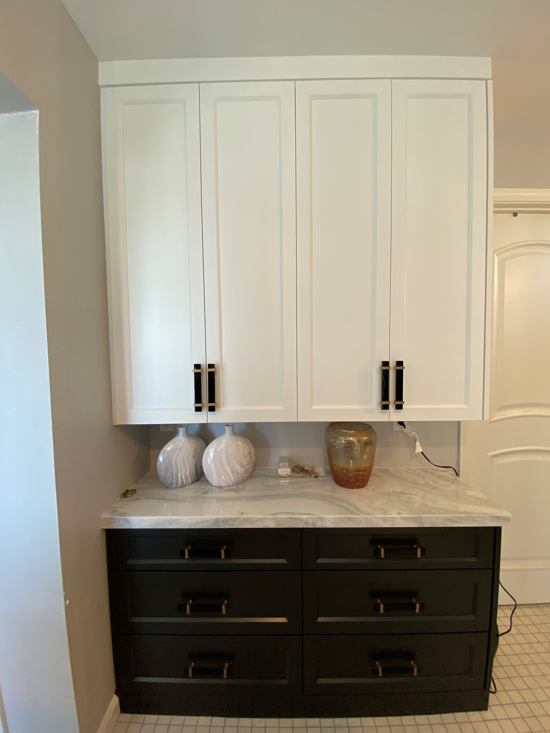White and black cabinets with marble countertop. Decorative vases and dark handles are on display.