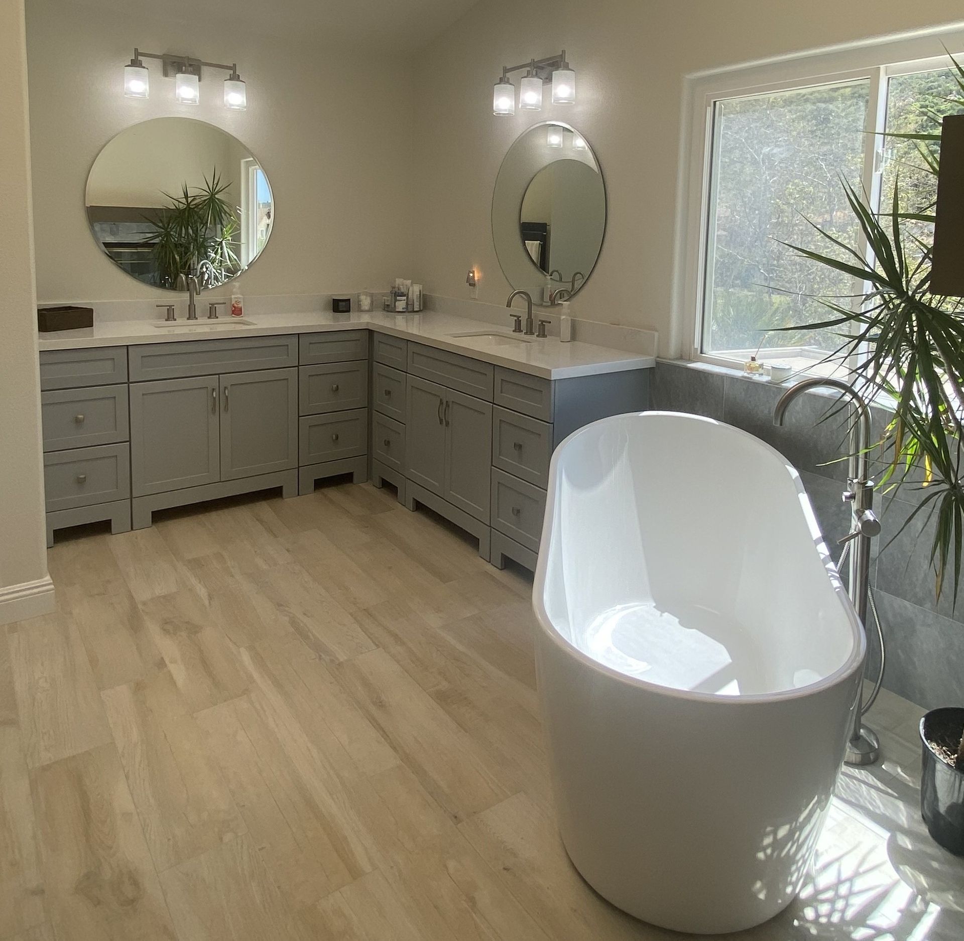 Modern bathroom with freestanding tub, double vanity, large window, and neutral color scheme.