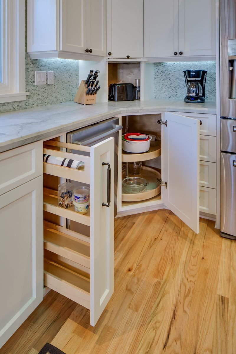 White kitchen corner with pull-out spice rack and lazy susan for accessible storage on wood floor.