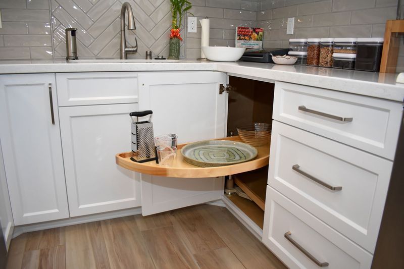 White kitchen cabinets with a corner cabinet featuring a pull-out lazy susan holding plates and glasses.