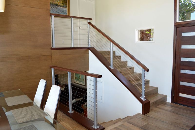 Wooden staircase with stainless steel cable railing and wood handrails, in a modern interior setting.