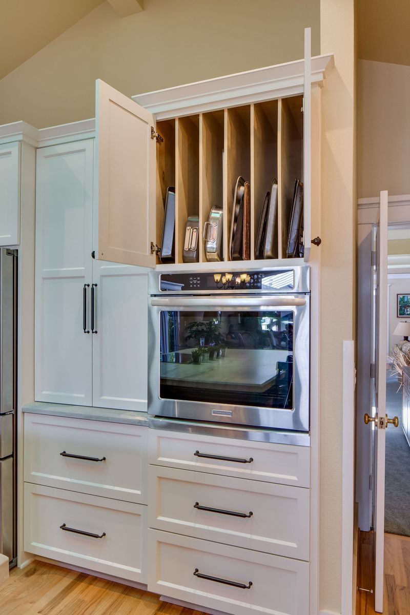 White kitchen cabinetry with oven and vertical storage, one door open.