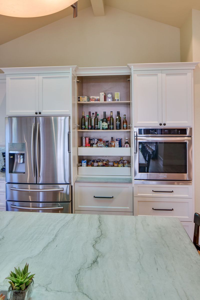 Kitchen with stainless steel appliances, white cabinets, built-in pantry, and oven.