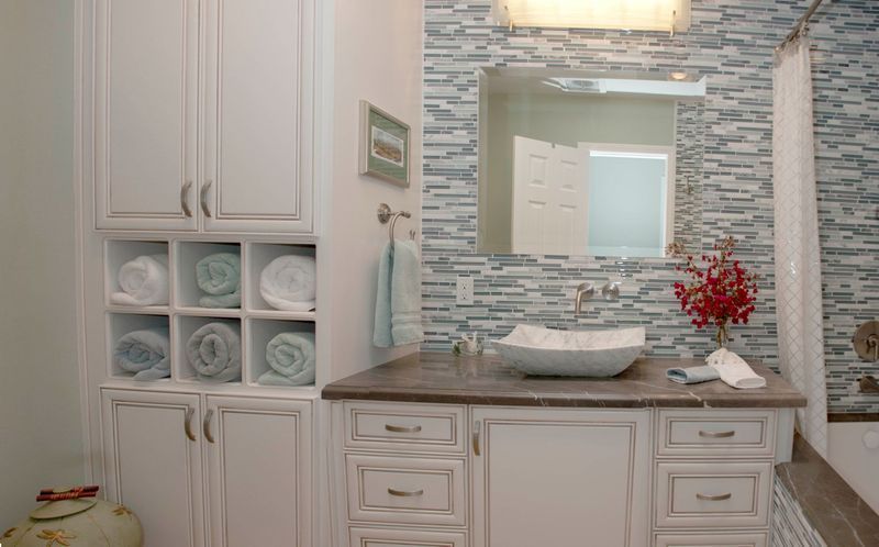 Bathroom with white cabinets, blue tile wall, vessel sink, towels, and red flowers.
