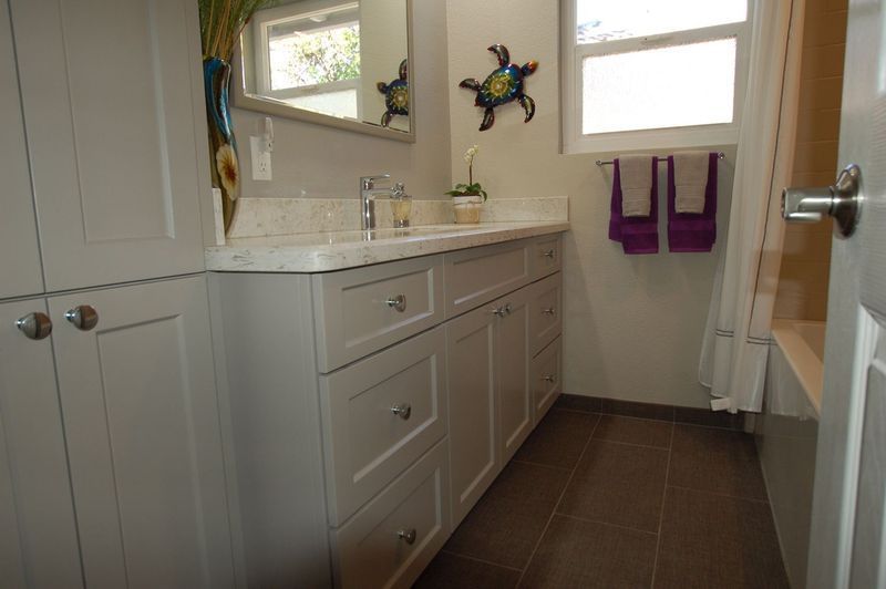 Bathroom with white cabinets, brown floor, and purple towels.