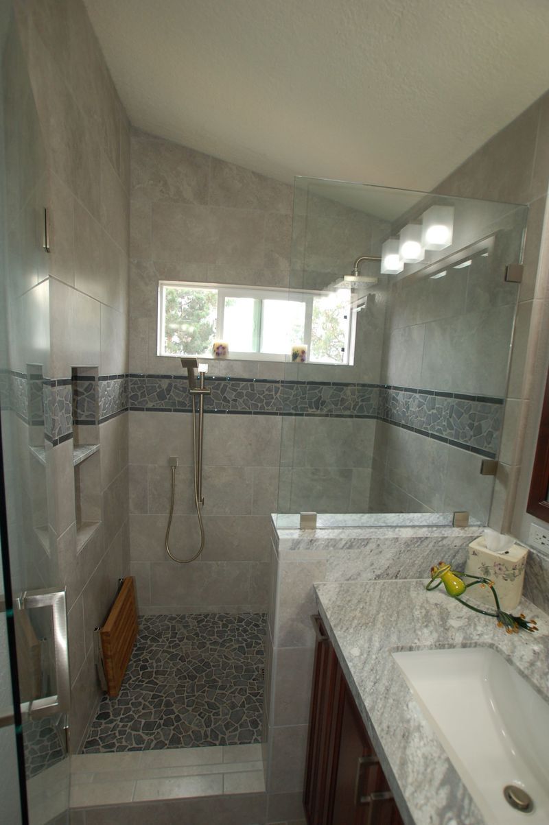 Bathroom shower with gray tiled walls, pebble floor, glass enclosure, vanity on right.