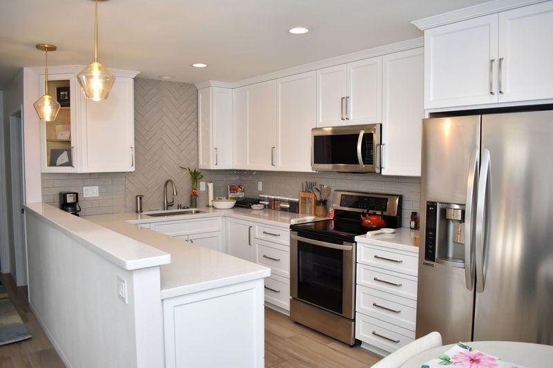 White kitchen with stainless steel appliances, white cabinets, and light gray backsplash.