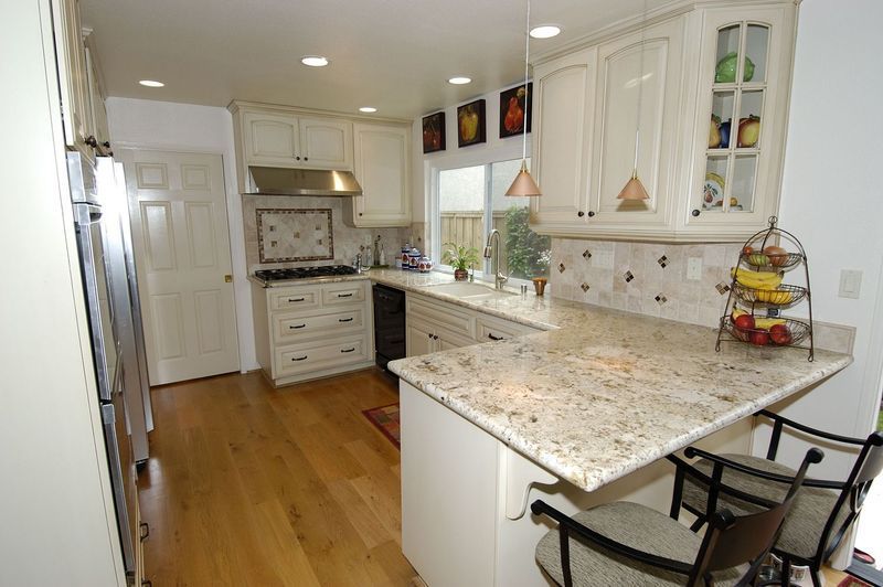 Kitchen with off-white cabinets, granite countertops, and hardwood floors. Includes a breakfast bar and stainless steel appliances.